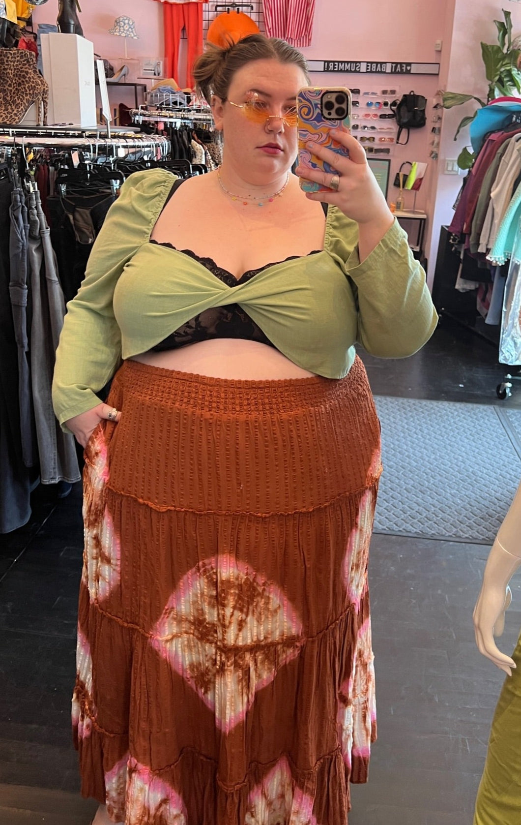 Half-body front view of a size 26 Pretty Little Thing sage green crop top with twist-bust detail and puff shoulders and sleeves styled with a rust brown skirt on a size 24 model.