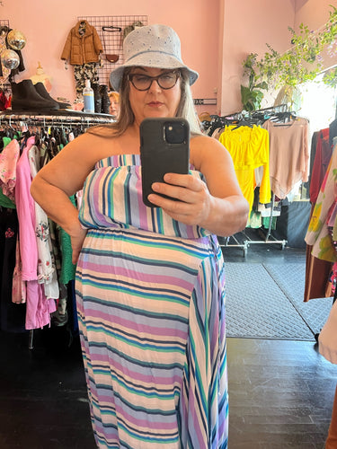 Front view of a size 22/24 Swimsuits for All blue, teal, purple, and white multi-stripe strapless maxi dress with drawstring bust detail styled with an eyelet bucket hat on a size 20/22 model.