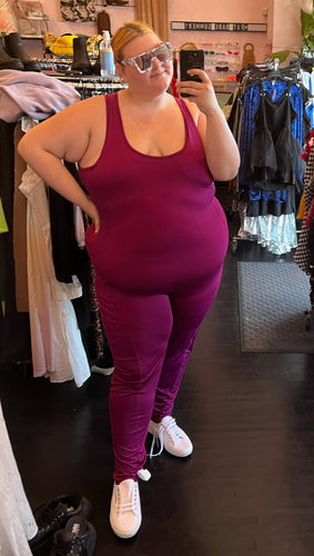 Full-body front view of a size 3X J. Dow Fitness magenta athletic jumpsuit styled with white sneakers and white block sunglasses on a size 22/24 model.