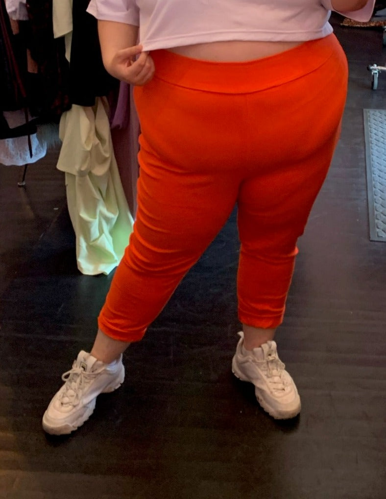 Front view of a pair of size 4 Fashion to Figure orange leggings styled with a white crop top and white sneakers on a size 22/24 model.