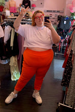 Load image into Gallery viewer, Additional full-body front view of a pair of size 4 Fashion to Figure orange leggings styled with a white crop top and white sneakers on a size 22/24 model.
