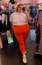 Load image into Gallery viewer, Full-body front view of a pair of size 4 Fashion to Figure orange leggings styled with a white crop top and white sneakers on a size 22/24 model.
