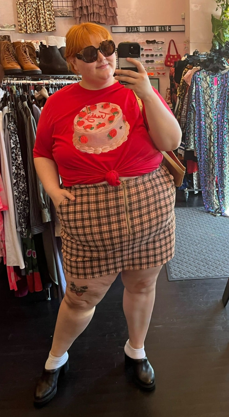 Full-body front view of a size 24W Wild Fable peach, red, and brown plaid mini skirt with zip up detail styled with a red graphic tee on a size 22/24 model.