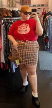Load image into Gallery viewer, Additional full-body front view of a size 24W Wild Fable peach, red, and brown plaid mini skirt with zip up detail styled with a red graphic tee on a size 22/24 model.
