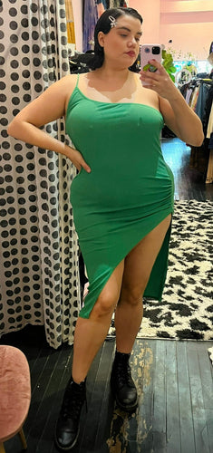 Full-body front view of a size 14 Pretty Little Thing kelly green asymmetrical high, high slit sexy midi dress styled with black combat boots on a size 14/16 model.