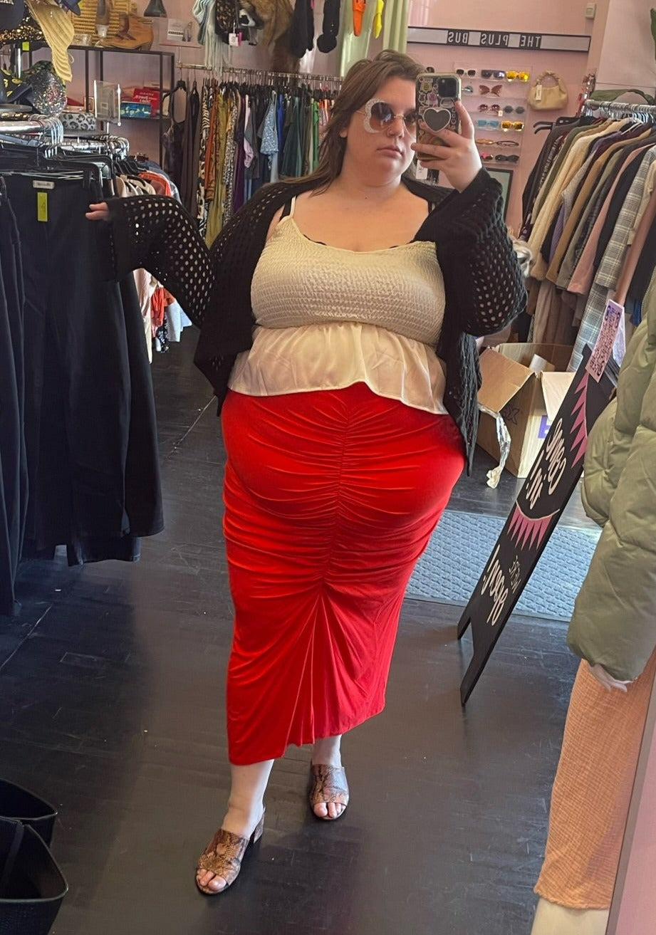 Full-body front view of a size 24 Eloquii bright red ruched-front maxi skirt styled with a cream-colored crop and black sweater on a size 24 model.
