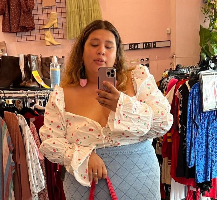 Front view of a size 28 Eloquii white puffed bell sleeve blouse with red and green cherry pattern styled with a denim mini skirt on a size 20/22 model.