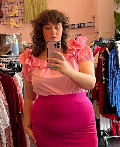 Front view of a size XL Malco Models peachy pink off-shoulder-optional ruffle neck short sleeve blouse styled tucked into a magenta pencil skirt on a size 14/16 model.