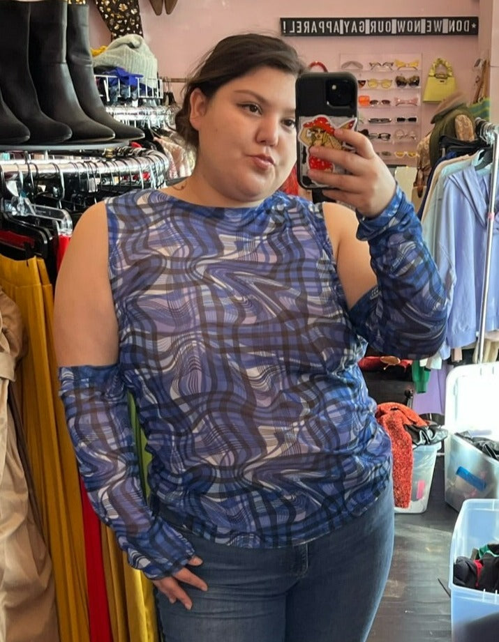 Close-up view of a size 18 ASOS blue, black, and white glitched plaid pattern futuristic-style mesh top with extreme cold shoulder and arm-warmer detail styled with jeans on a size 16 model.