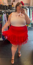 Load image into Gallery viewer, Full-body front view showing off the tiers of a size 24 Eloquii red ruffle-tiered mini skirt styled with a baby pink pussybow blouse and snakeprint heels on a size 24 model.
