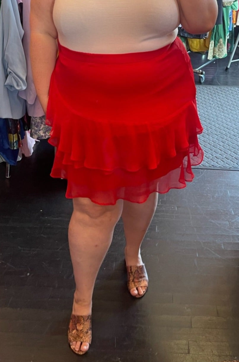 Close front view of a size 24 Eloquii red ruffle-tiered mini skirt styled with a baby pink blouse and snakeprint heels on a size 24 model.