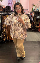 Load image into Gallery viewer, Full-body front view of a size XXL The Lullaby Club neutral tone floral blouse with fabric buttons, puff sleeves, and a baby doll shape styled with khaki trousers and floral glasses on a size 14/16 model.
