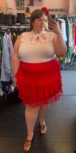 Load image into Gallery viewer, Full-body front view of a size 24 Eloquii red ruffle-tiered mini skirt styled with a baby pink pussybow blouse and snakeprint heels on a size 24 model.
