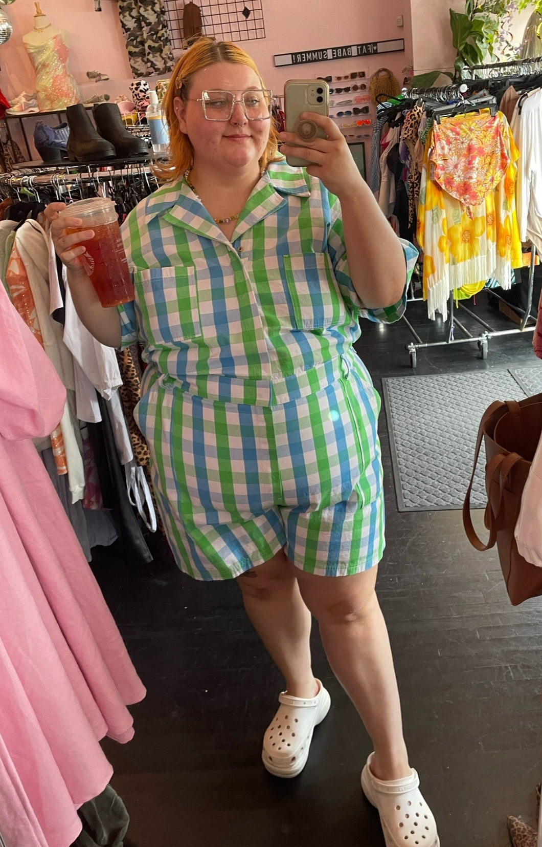 Full-body front view of a size 6X Big Bud Press green and blue checkered plaid short sleeve romper styled with white Crocs on a size 22/24 model.