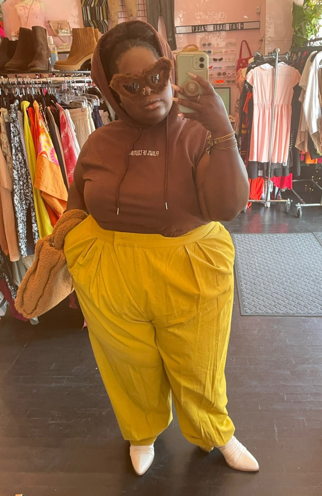 Full-body front view of a size 2X Shein X collab with Flaws of Couture chocolate brown tank hoodie styled with yellow trousers, white boots, and a teddy purse on a size 22/24 model.