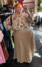 Load image into Gallery viewer, Full-body front view of a size XXL The Lullaby Club neutral tone floral blouse with fabric buttons, puff sleeves, and a baby doll shape styled tucked into a khaki elastic waist skirt on a size 22/24 model.
