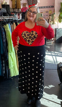 Load image into Gallery viewer, Full-body front view of a size 2 Torrid red lightweight sweater with a leopard pattern heart and ribbed cuffs styled tucked into a black and white polka dot sweater skirt with boots on a size 20/22 model.
