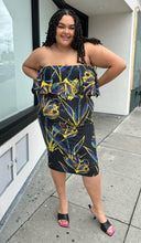 Load image into Gallery viewer, Additional full-body front view of a size 3X Rue 107 black strapless ruffle bust bodycon column dress with all-over yellow, teal, and royal blue paint splatter pattern styled with black heels on a size 18/20 model. The photo is taken outside in natural lighting.
