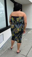 Load image into Gallery viewer, Full-body back view of a size 3X Rue 107 black strapless ruffle bust bodycon column dress with all-over yellow, teal, and royal blue paint splatter pattern styled with black heels on a size 18/20 model. The photo is taken outside in natural lighting.
