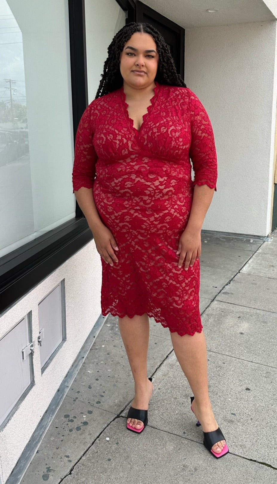 Full-body front view of a size 2 (18/20) Kiyonna bright red all-over lace bodycon dress with v-neck and scalloped edge styled with black heels on a size 18/20 model.
