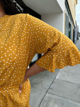 Load image into Gallery viewer, Close up view of the mustard color and very subtle bell sleeve detail of a size 20 Boohoo mustard yellow faux wrap mini dress with white polka dots, a ruffle hem, and a subtle bell sleeve on a size 18/20 model.
