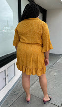 Load image into Gallery viewer, Full-body back view of a size 20 Boohoo mustard yellow faux wrap mini dress with white polka dots, a ruffle hem, and a subtle bell sleeve styled with black heels on a size 18/20 model.

