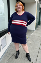Load image into Gallery viewer, Full-body front view of a size 22/24 Eloquii x Katie Sturino navy blue ribbed knit sweater dress with red and white varisty stripes and a red and white v-neck stripe styled with black boots on a size 22/24 model. The photo is taken outside in natural lighting.
