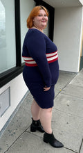 Load image into Gallery viewer, Full-body side view of a size 22/24 Eloquii x Katie Sturino navy blue ribbed knit sweater dress with red and white varisty stripes and a red and white v-neck stripe styled with black boots on a size 22/24 model. The photo is taken outside in natural lighting.
