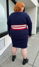 Load image into Gallery viewer, Full-body back view of a size 22/24 Eloquii x Katie Sturino navy blue ribbed knit sweater dress with red and white varisty stripes and a red and white v-neck stripe styled with black boots on a size 22/24 model. The photo is taken outside in natural lighting.
