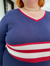 Load image into Gallery viewer, Close up view of the ribbing and varsity stripe on a size 22/24 Eloquii x Katie Sturino navy blue ribbed knit sweater dress with red and white varisty stripes and a red and white v-neck stripe on a size 22/24 model. The photo is taken outside in natural lighting.
