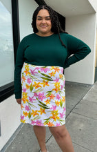 Load image into Gallery viewer, Front view of a size 2X Unicorn Tears vintage white midi skirt with pink, yellow, and green floral pattern styled with a deep emerald long sleeve top on a size 18/20. The photo is taken outside with natural lighting.
