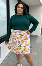 Load image into Gallery viewer, Additonal front view of a size 2X Unicorn Tears vintage white midi skirt with pink, yellow, and green floral pattern styled with a deep emerald long sleeve top on a size 18/20. The photo is taken outside with natural lighting.
