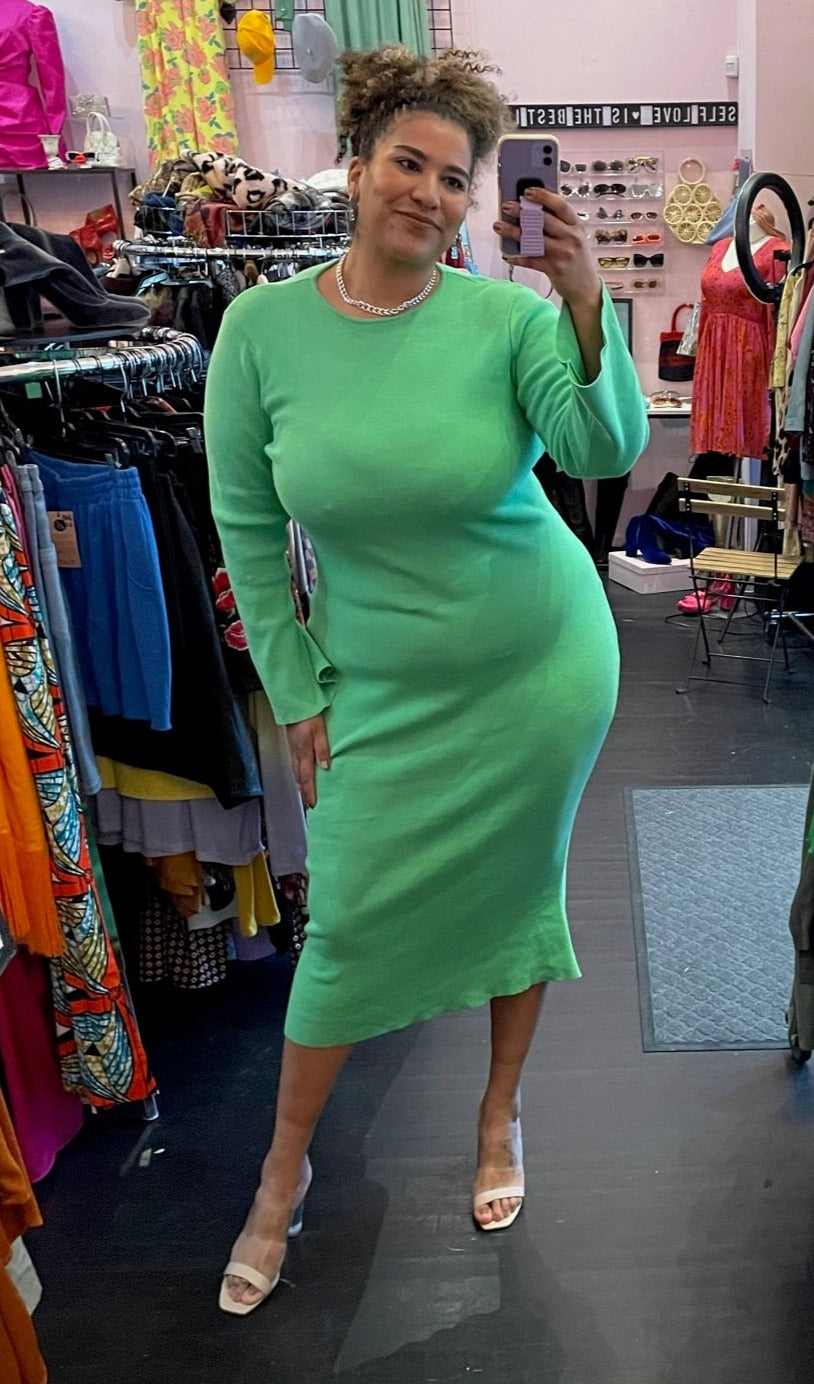 Full-body front view of a size L/XL (fits like 16/18) vibrant seafoam green ribbed knit sweater dress with a higher neckline and an open back styled with tan heels and a chain on a size 16/18 model. The photo is taken inside under overhead lighting.