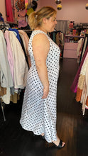 Load image into Gallery viewer, Full-body side view of a size 18 ASOS white sleeveless maxi dress with black polka dots and a ruched slit detail at the hem styled with black heels on a size 14/16 model. The photo is taken inside in front of a window, combining natural lighting and overhead lighting.
