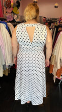 Load image into Gallery viewer, Full-body back view showing off the keyhole back of a size 18 ASOS white sleeveless maxi dress with black polka dots and a ruched slit detail at the hem styled with black heels on a size 14/16 model. The photo is taken inside in front of a window, combining natural lighting and overhead lighting.
