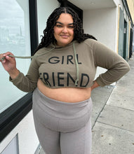 Load image into Gallery viewer, Front view of a size 2X Onuolayichu olive green cropped hoodie that reads, &quot;GIRLFRIEND&quot; styled with gray leggings on a size 18/20 model.
