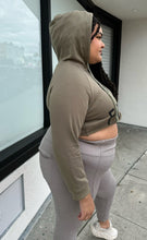 Load image into Gallery viewer, Side view of a size 2X Onuolayichu olive green cropped hoodie that reads, &quot;GIRLFRIEND&quot; styled with the hood up and gray leggings on a size 18/20 model.
