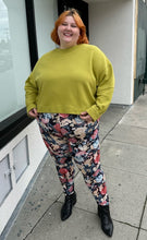 Load image into Gallery viewer, Full-body front view of a pair of size 3X Miss Look muted multicolor floral leggings styled with a chartreuse crewneck and black boots on a size 22/24 model.
