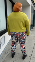 Load image into Gallery viewer, Full-body back view of a pair of size 3X Miss Look muted multicolor floral leggings styled with a chartreuse crewneck and black boots on a size 22/24 model.
