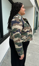 Load image into Gallery viewer, Side view of a size 2X Forever 21 green camo denim jacket with snap closure buttons styled open over a black dress on a size 18/20 model.
