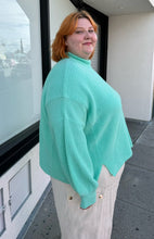 Load image into Gallery viewer, Side view of a size 18 ASOS cyan teal thick knit mockneck oversized sweater styled over cream pants on a size 22/24 model.
