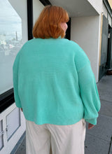 Load image into Gallery viewer, Back view of a size 18 ASOS cyan teal thick knit mockneck oversized sweater styled over cream pants on a size 22/24 model.
