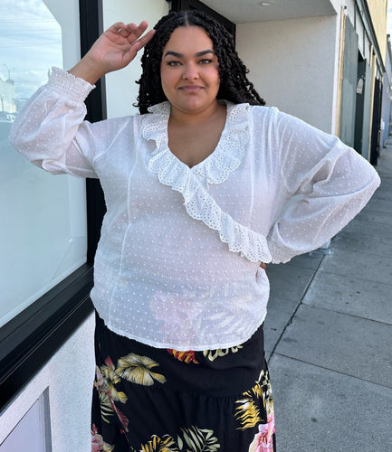 Front view of a size 4X SHEIN white sheer-leaning blouse with ruffled eyelet collar, all-over swiss dots, and smocked cuffs styled with a black wrap skirt on a size 18/20 model.