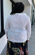 Load image into Gallery viewer, Back view of a size 4X SHEIN white sheer-leaning blouse with ruffled eyelet collar, all-over swiss dots, and smocked cuffs styled with a black wrap skirt on a size 18/20 model.
