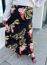 Load image into Gallery viewer, Front view of a size 4X SHEIN black tiered maxi skirt with pink, yellow, and green tropical floral pattern maxi skirt styled with a white blouse and black heels on a size 18/20 model.
