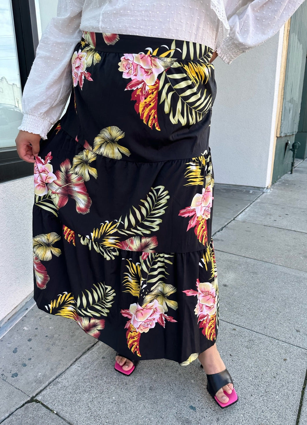 Front view of a size 4X SHEIN black tiered maxi skirt with pink, yellow, and green tropical floral pattern maxi skirt styled with a white blouse and black heels on a size 18/20 model.