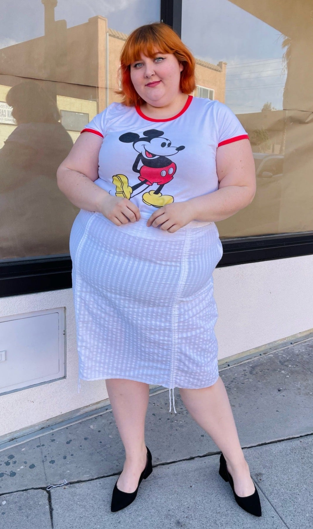 Full body front view of a white vertical striped midi skirt with optional side ruching styled with a white and red Mickey Mouse tee and black pumps on a size 22/24 model.
