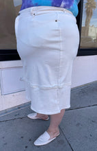 Load image into Gallery viewer, Side view of a size L Universal Standard white deconstructed denim midi skirt styled with a blue and purple tie dye tee and white slides on a size 22/24 model.
