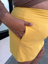 Load image into Gallery viewer, Close up view of the zipper pocket details on a size 2X Alder sunshine yellow mini skirt with a small front-side slit detail on a size 18/20 model.
