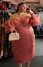 Load image into Gallery viewer, Front view of a size 24 ASOS peachy pink lace sheath dress with a corset-style bodice and oversized ruffle bust and sleeves with puff sleeves on a size 22 model. The photo is taken inside under overhead lighting.
